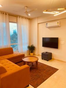 a living room with a couch and a table and a tv at HomeyStays 2BHK Lakeside walk in Rāi +15 photos