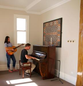 a man sitting at a piano with a woman playing a guitar at Verandahs Parkside Lodge in Auckland