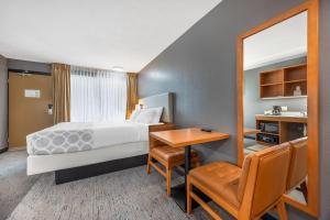 a hotel room with a bed and a desk and a mirror at Suburban Studios Branson On The Strip in Branson