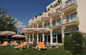 a group of chairs and umbrellas in front of a building at Két Korona Konferencia és Wellness Hotel in Balatonszárszó