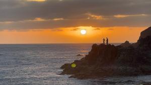 Dos personas pescando en una roca en el océano al atardecer en Sardina Beach Retreat, en Gáldar
