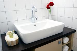 lavabo blanco en el baño con una flor roja en Apartmenthotel Quartier M, en Leipzig