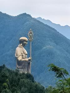 une statue d'un homme tenant une pancarte devant une montagne dans l'établissement Jiuhua Mountain Tanfeng Resort Homestay 远眺山景大佛 九华山潭风民宿, à Miaoqian