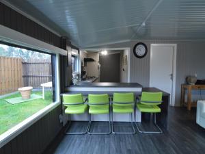a kitchen with a bar with green chairs at Modern waterfront chalet in Geel