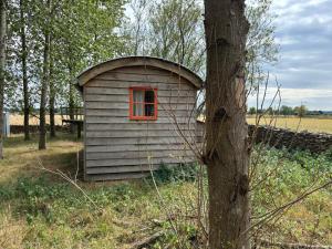 a small house with a red window next to a tree at Secluded off grid Shepherd's Hut in Minchinhampton