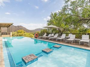 een zwembad met ligstoelen en een parasol bij Shepherds Tree Game Reserve in Pilanesberg