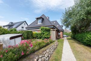 a house with a stone retaining wall and flowers at Sylter Wohlfühlnest, App 2 in Wenningstedt
