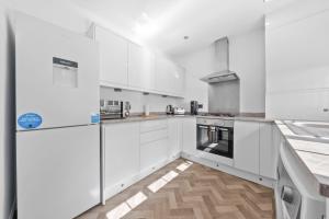 a white kitchen with white appliances and a wooden floor at Kirkstyle Cottage in Coatbridge
