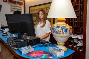 eine Frau, die an einem Computer an einem Schreibtisch mit einer Lampe arbeitet in der Unterkunft Hotel Neapolis in Neapel