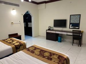 ein Schlafzimmer mit zwei Betten und einem Schreibtisch mit Fernseher in der Unterkunft Twilight Hotel Al-Hail in Muscat