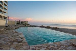 una gran piscina junto a una playa con sombrillas en Top-Floor Rosarito Penthouse with Ocean Views, Sauna, Jacuzzis and Pools, en Rosarito