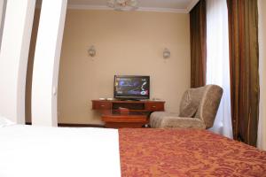 um quarto de hotel com uma cama, uma televisão e uma cadeira em ABAI INN - Nursaya em Taraz