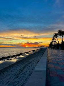 a beach with palm trees and a sunset in the background at Estilo y relax junto al mar in Santa Pola