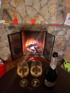 two glasses and a bottle of wine on a table with a fireplace at Chalé Garden da Mantiqueira in Monte Verde