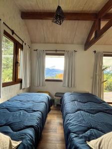 two beds in a room with two windows at Casa en la Montaña, Casa Chucao in El Bolsón