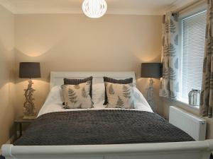 una camera da letto con un letto bianco con cuscini e una finestra di Elm Tree Cottage a Foxholes