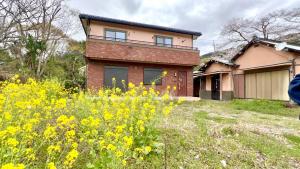 a house with a field of yellow flowers in front of it at Orbit ALDERAN-Home Stay in Matsuda