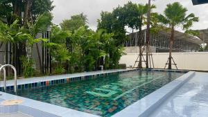 a swimming pool with palm trees and a building at UPMOON Hotel Chalong Phuket in Ban Suan