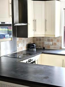 a kitchen with white cabinets and a black counter top at Cosy 3 Bedroom Bungalow with Private Parking and Rear Garden in Milton Keynes