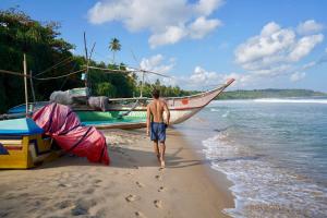 a man walking on the beach next to a boat at The Cabana Hotel Hiriketiya in Dickwella