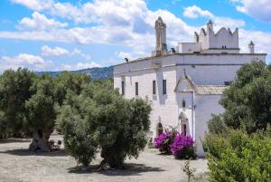 an old white building with trees in front of it at Masseria Palombara Grande in Ostuni