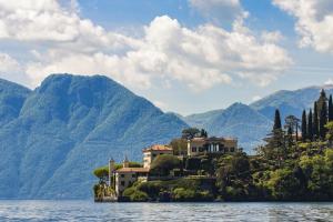 a house on a island in the water with mountains at La terrazza di Marta in Varenna