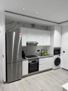 une cuisine avec des armoires blanches et un réfrigérateur en acier inoxydable dans l'établissement Apartamento AEROPUERTO12, à Coslada