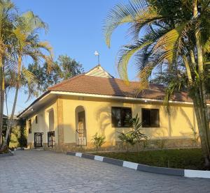 ein gelbes Haus mit Palmen davor in der Unterkunft Rhovee Arusha in Arusha