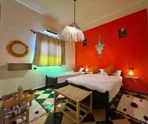 a bedroom with two beds and a red wall at Riad Dar Sahara - Panoramic Rooftop & Outdoor Shower in Nkob