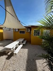 a patio with two picnic tables in front of a yellow house at Casa Caia - simple rooms and studios at studenthouse in Willemstad