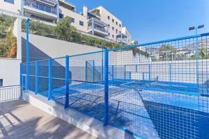 ein Tennisplatz mit einem blauen Zaun neben einem Gebäude in der Unterkunft Ático 90m de terraza, jacuzzi privado y cargador de coche eléctrico en Cabria, Almuñecar in Almuñécar