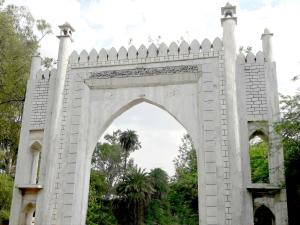 einen Torbogen in einem Park mit einem weißen Zaun in der Unterkunft Taj Castle A Boutique Homestay in Agra