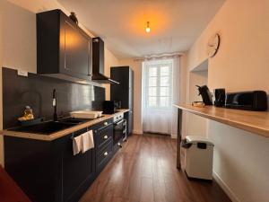 eine Küche mit schwarzen Schränken und einem Holzboden in der Unterkunft Maison Hythou de ville 6 personnes in Thouars