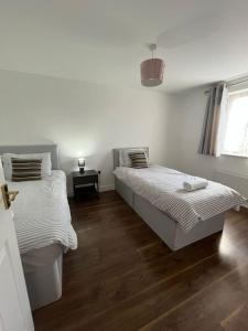 two beds in a room with white walls and wooden floors at Trowbridge House Long Stays Free Parking and Wifi in Swindon