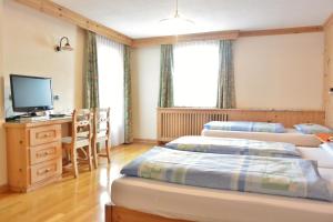 a room with three beds and a desk and a television at Hotel Garnì al Plan in Livigno