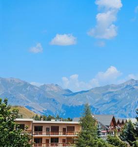 a building with mountains in the background with blue sky and clouds at Appartement Pied Des Pistes in La Toussuire