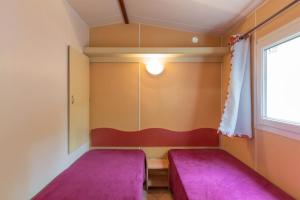 two beds in a small room with purple cushions at Camping Midi - mobil home 4-6 pers in Vallon-Pont-dʼArc