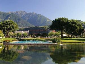 a golf course with a pond with mountains in the background at M-Loft merangardenvilla in Merano