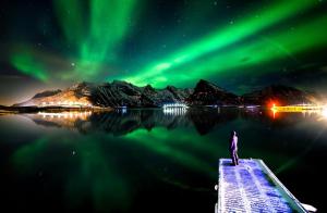 a person standing on a pier watching the northern lights at Lydersen Rorbuer Budget Hostel & Private Apartments in Fredvang