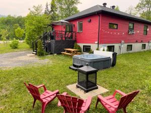 a group of chairs and a grill in front of a red house at Chalet des Érables in Petite-Rivière-Saint-François