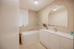 a white bathroom with a tub and a sink and a mirror at Casa Agonis in Geographe +33 photos