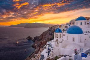 a sunset over a group of white buildings on a cliff at Oia Luxury villaes vacations in Oia