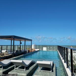 a swimming pool with chairs and the ocean in the background at Lindo Flat no Jardim Oceania - Get One in João Pessoa