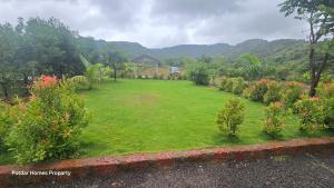 un champ d'herbe avec une maison en arrière-plan dans l'établissement Potdar holiday home & risort, à Chandoli