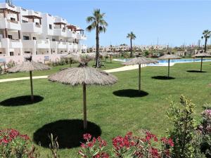 a group of straw umbrellas in the grass near a hotel at Apartamento moderno con piscina, a 500m de la playa, San Juan de los Terreros - ES-376-41 in Pulpí +6 photos