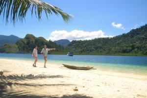 two people standing on a beach with a boat at Sumatra Ecolodge in Sungaipisang
