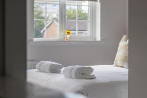 a white bedroom with towels on a bed with a window at Modern 2-Bedroom Home near Glasgow & Edinburgh in Airdrie