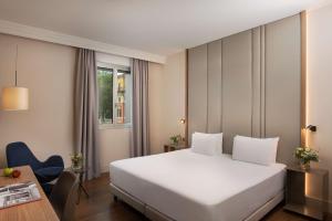 a hotel room with a white bed and a desk at NH Bologna De La Gare in Bologna +61 photos