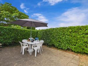 a table and chairs with an umbrella in front of a hedge at Piscine commune, terrasse, maison pour 5 in Saint-Vincent-sur-Jard