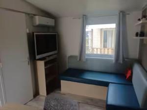 Una pequeña habitación con un sofá azul y una ventana. en Mobil home tout confort, en Narbona